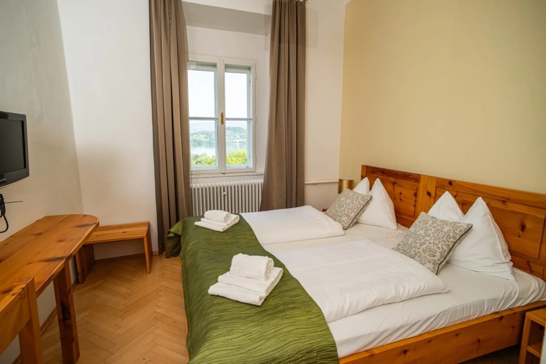 Doppelzimmer mit Schreibtisch, Fernseher und Fenster mit Blick auf grüne Hügel