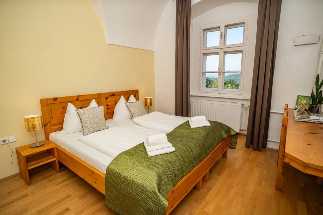Doppelzimmer mit Holzbett, grüner Tagesdecke und Fenster mit Blick ins Grüne