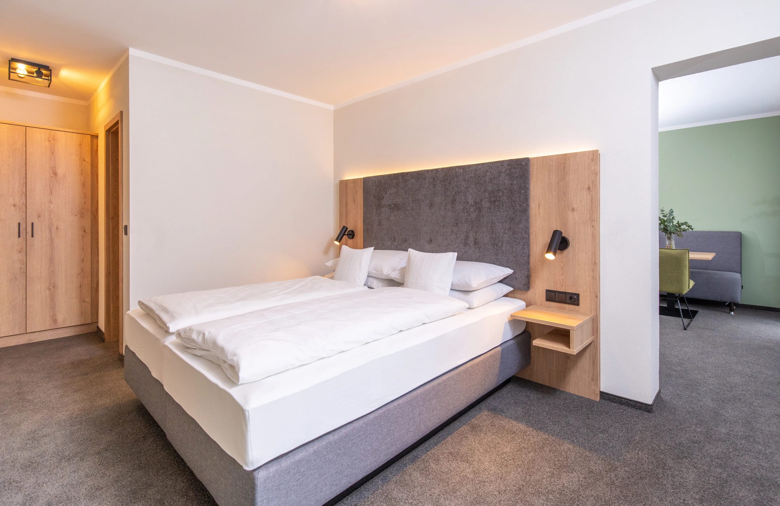 Schlafzimmer der Suite mit breitem Bett, indirekter Beleuchtung und offenem Durchgang zum Wohnbereich