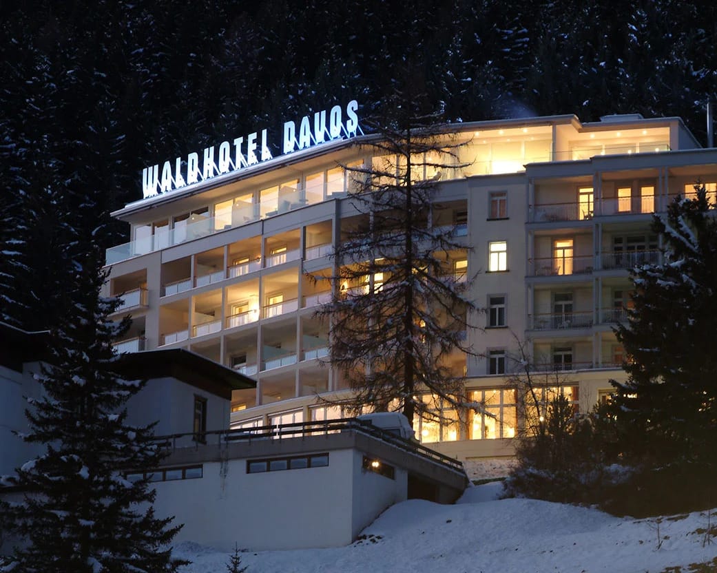 Beleuchtete Hotelfassade mit Leuchtschriftzug auf dem Dach bei Nacht im Schnee