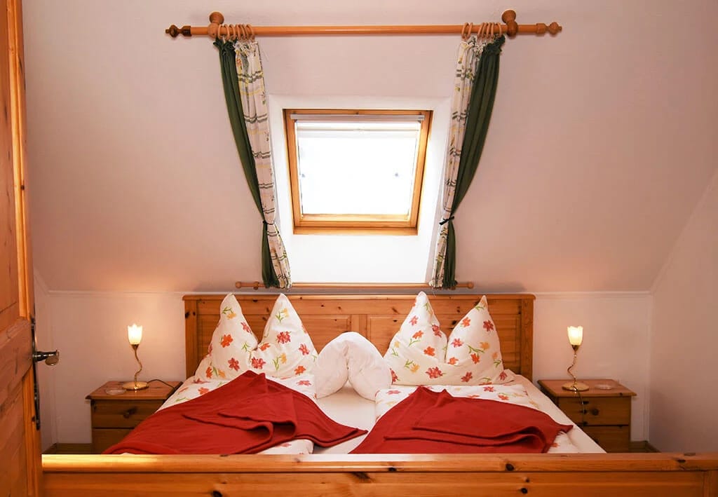 Zimmer mit Doppelbett aus hellem Holz, roten Kissenakzenten und Dachfenster