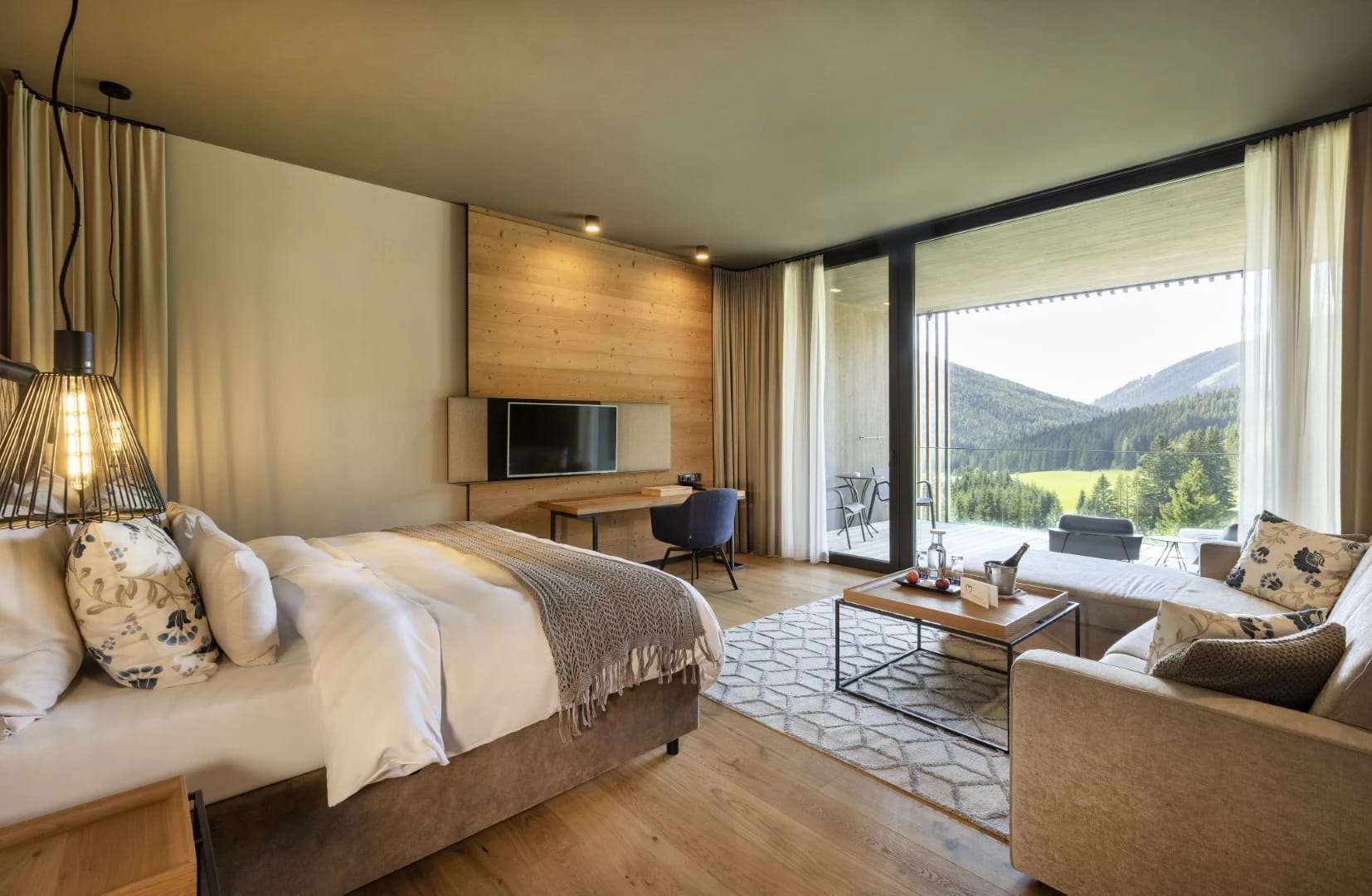 Zimmer mit Doppelbett, Schreibtisch, Sitzsessel und Terrassentür mit Blick auf die Berge