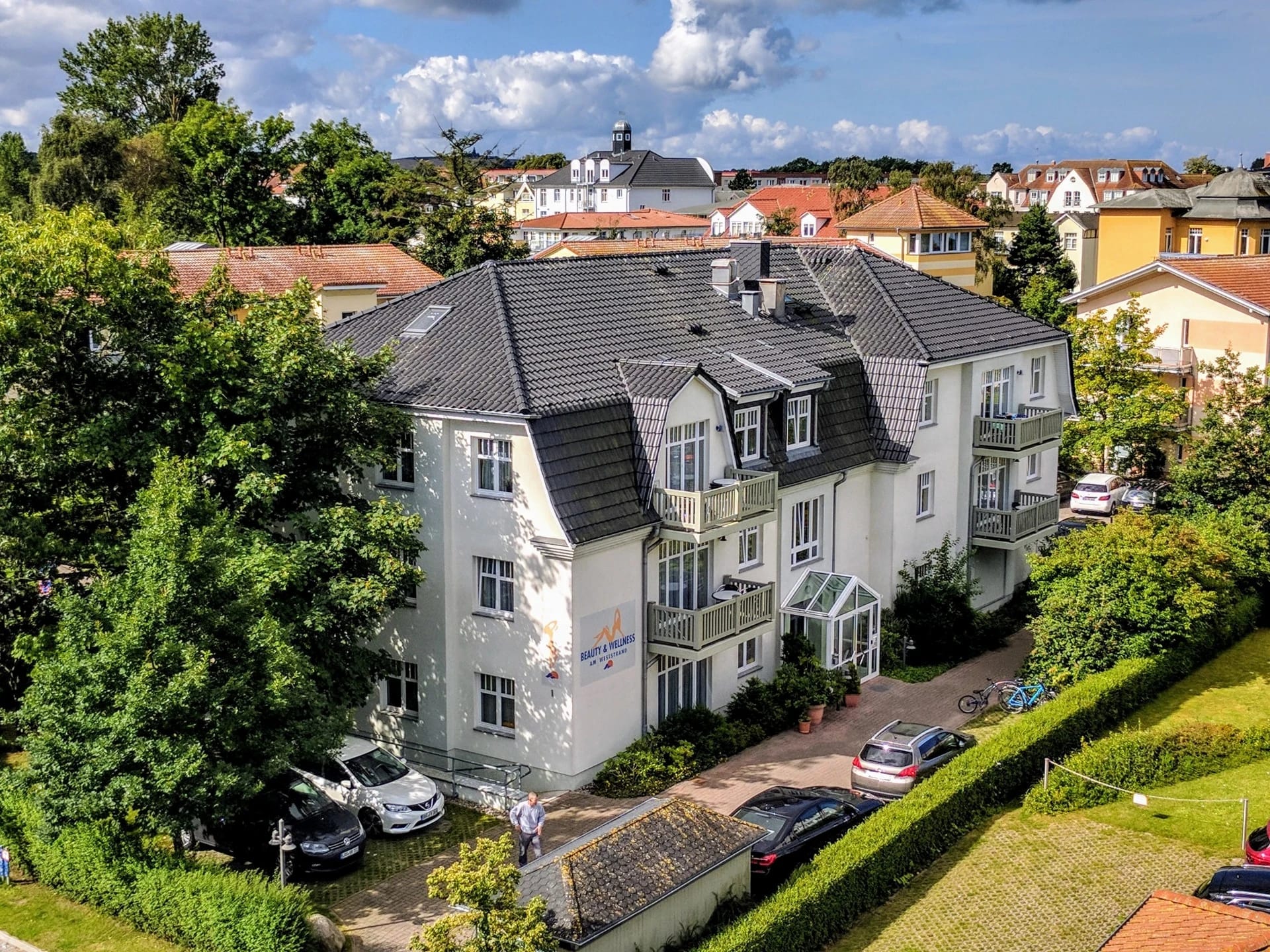 Ansicht des weißen Apartmenthauses mit Satteldach und Garten von oben