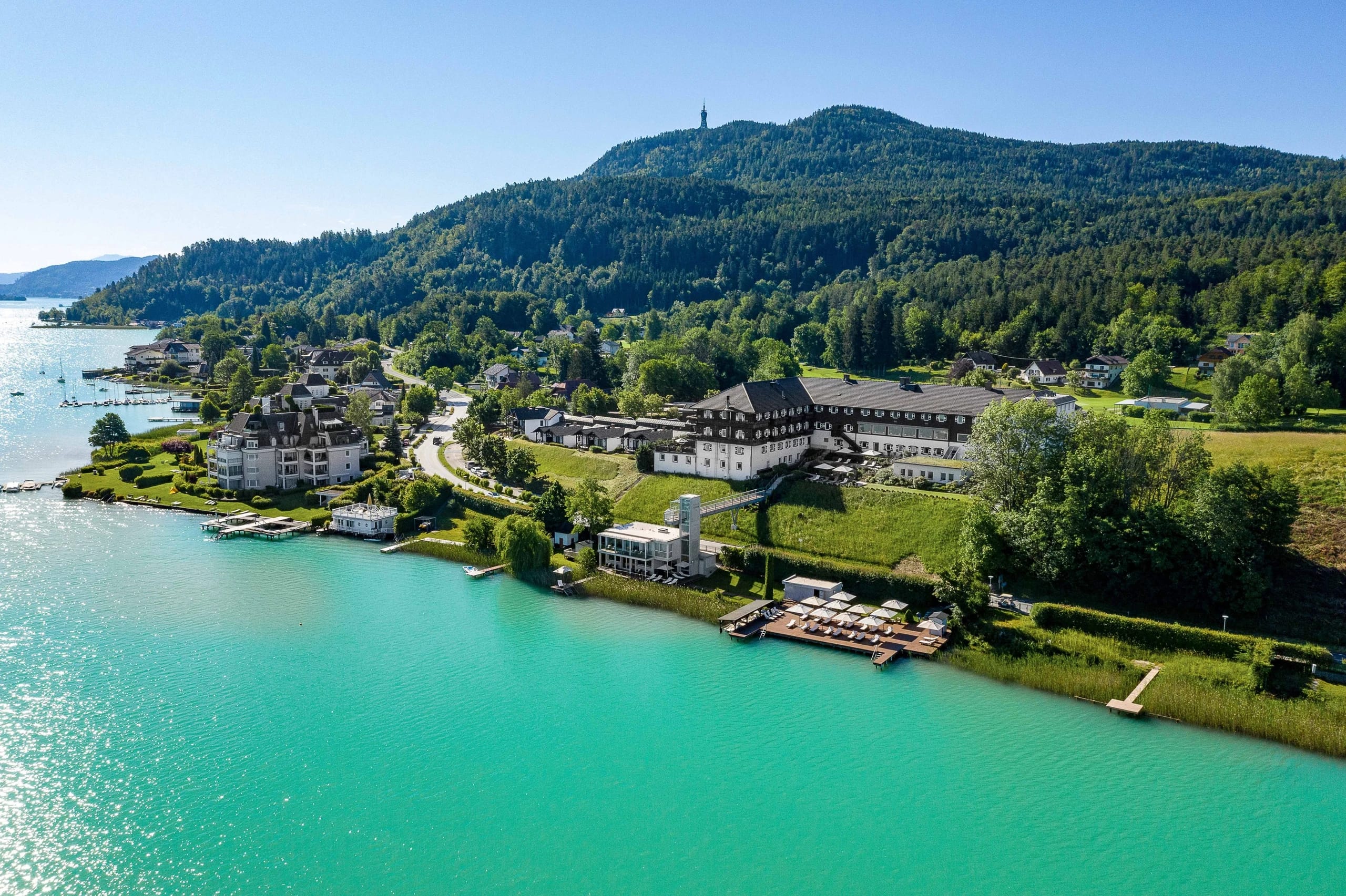 Luftaufnahme des Resorts am Seeufer mit bewaldeten Hügeln im Hintergrund