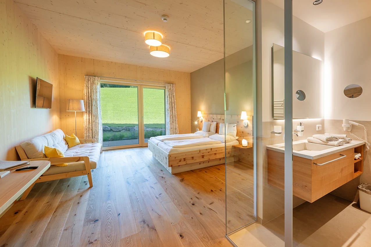 Zimmer mit Doppelbett aus Zirbenholz und offenem Bad hinter Glas