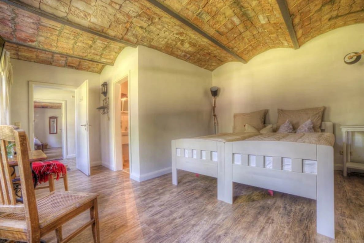 Schlafzimmer mit weißem Bett unter gewölbter Ziegeldecke und Holzdielen