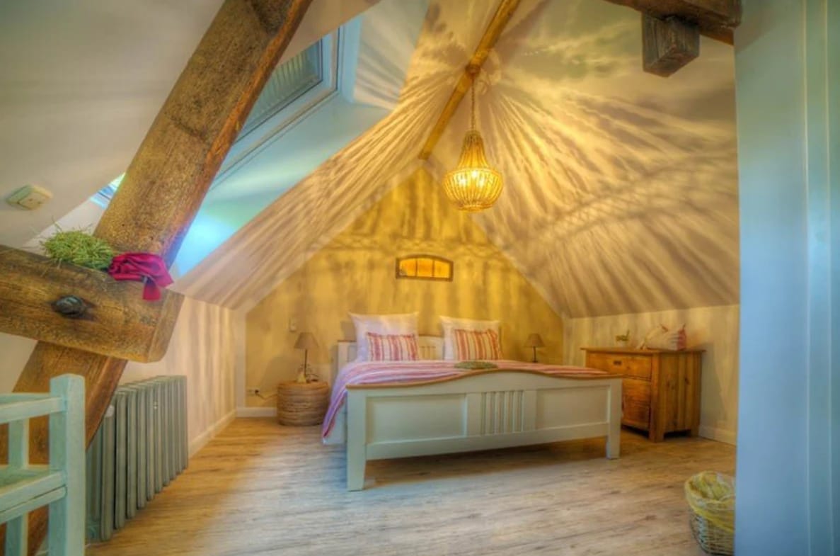 Dachgeschosszimmer mit Himmelbett, Holzbalken und Kronleuchter