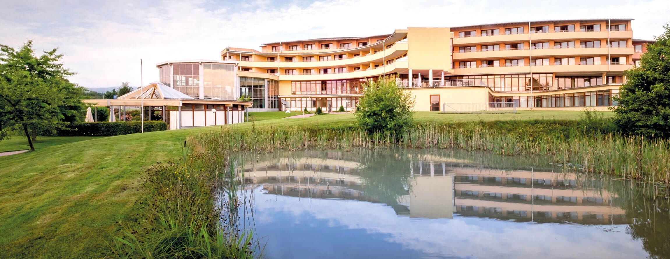 Hotelgebäude mit Balkonreihen, gespiegelt in einem Teich in der Parkanlage
