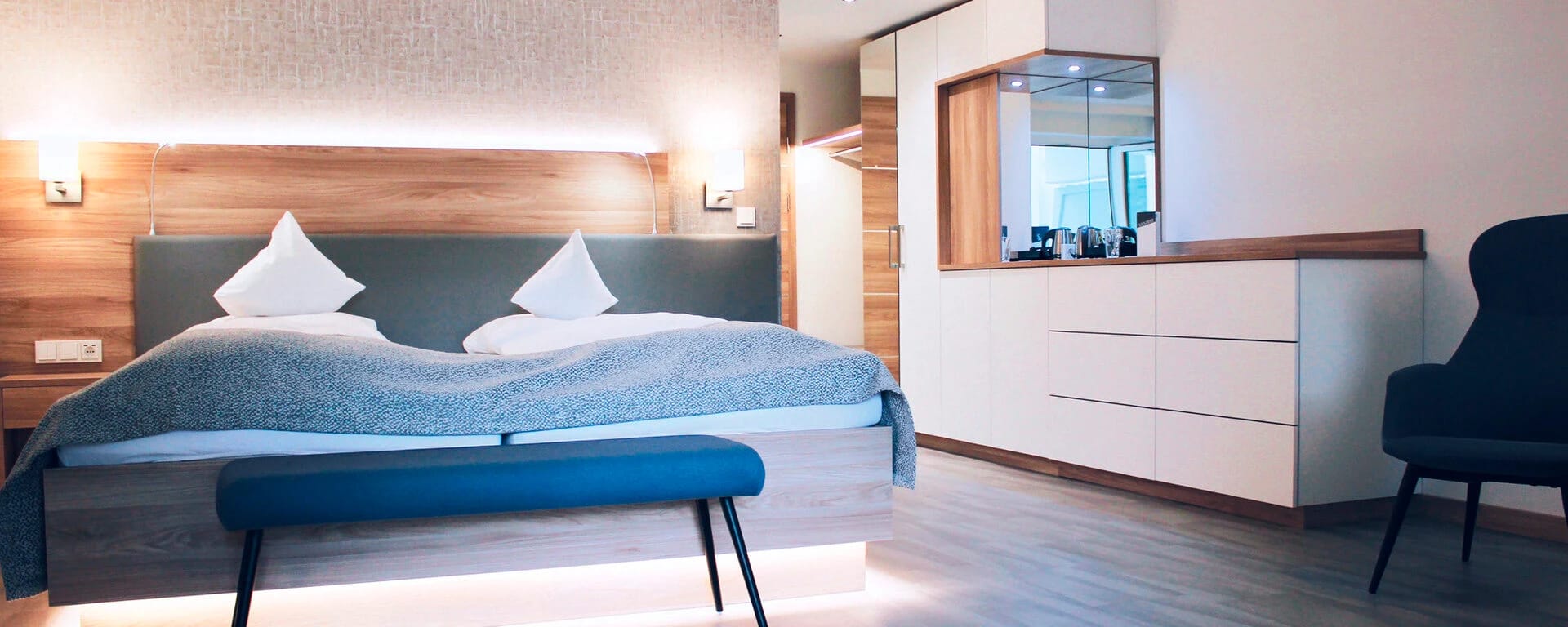 Modernes Doppelzimmer mit Holzwand hinter dem Bett, blauer Sitzbank und weißem Schrank