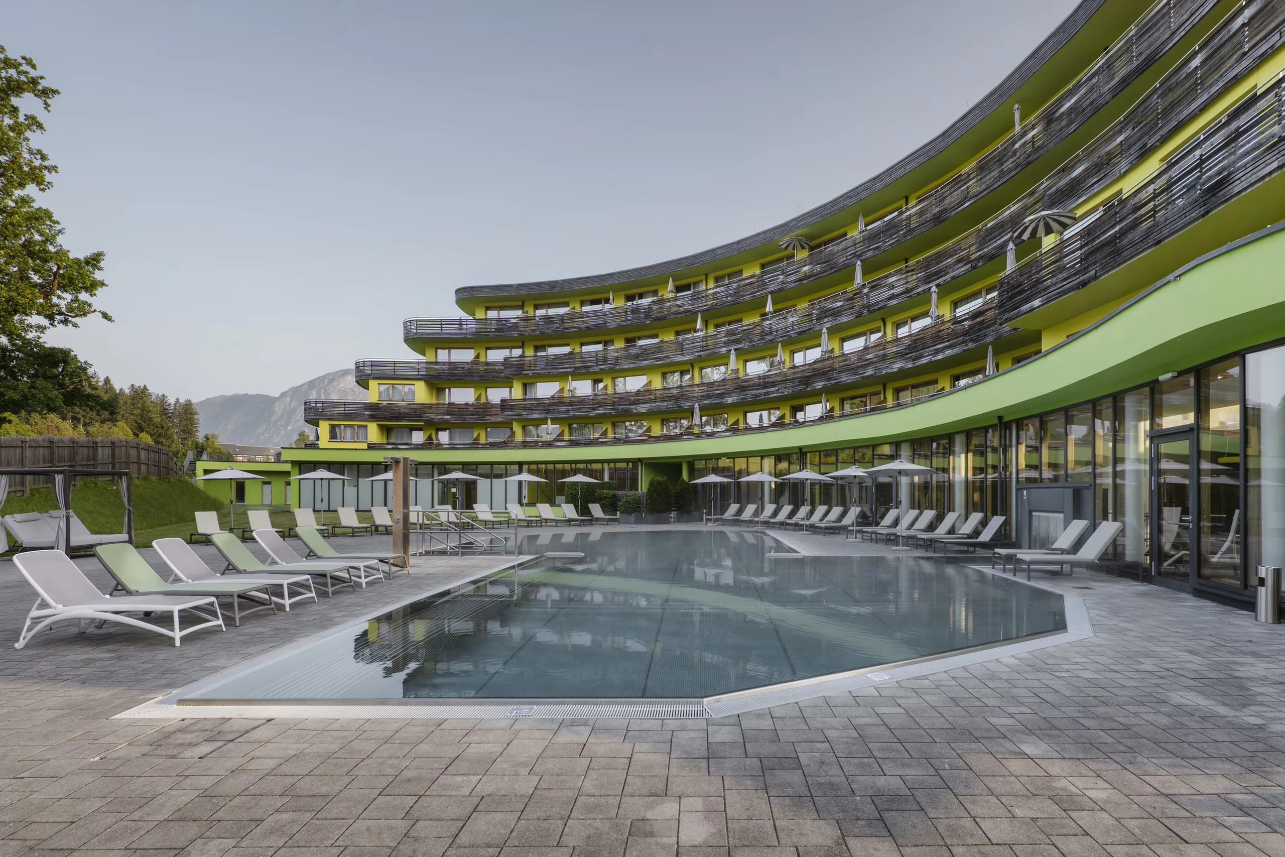 Außenbereich mit gepflasterter Terrasse, Liegen und Blick auf die Hotelfassade mit Balkonen