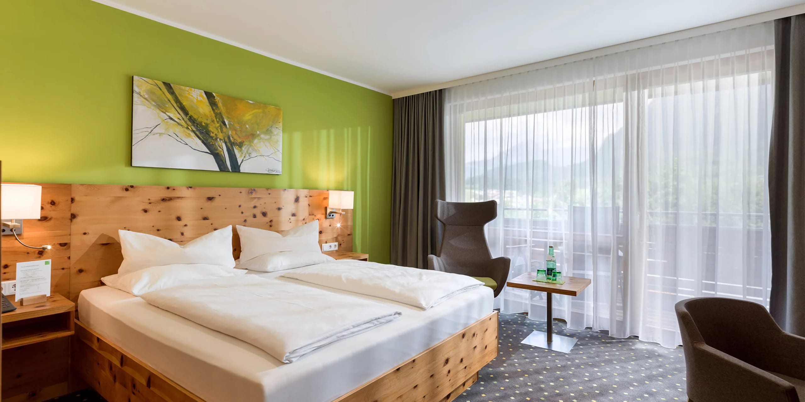 Doppelzimmer mit grüner Wand, Holzbett aus Zirbenholz und Sitzecke am Fenster