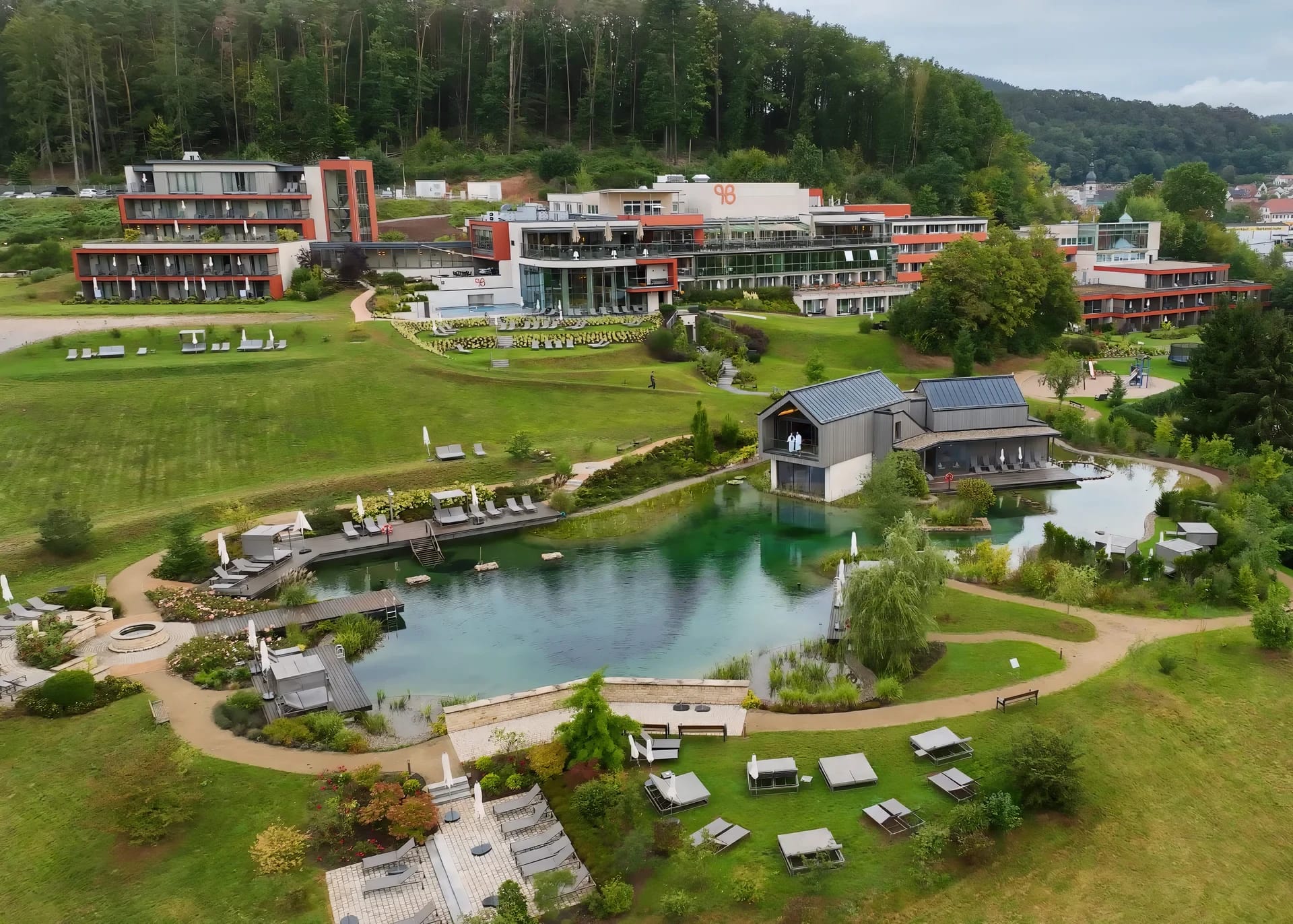 Luftaufnahme der Resortanlage mit Naturbadeteich, Liegeflächen und umliegendem Wald