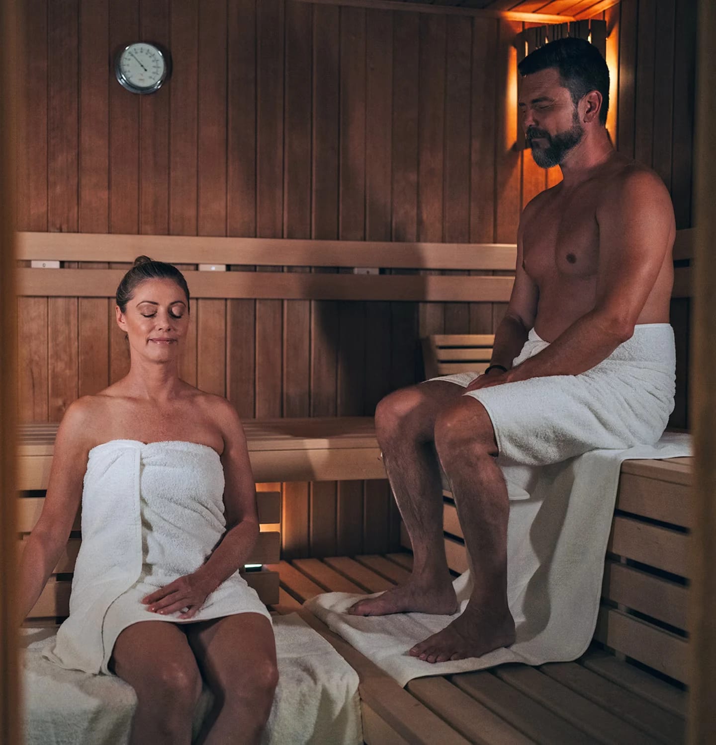 Holzsauna mit umlaufenden Bänken, zwei Gäste in Handtücher gehüllt auf den Bänken