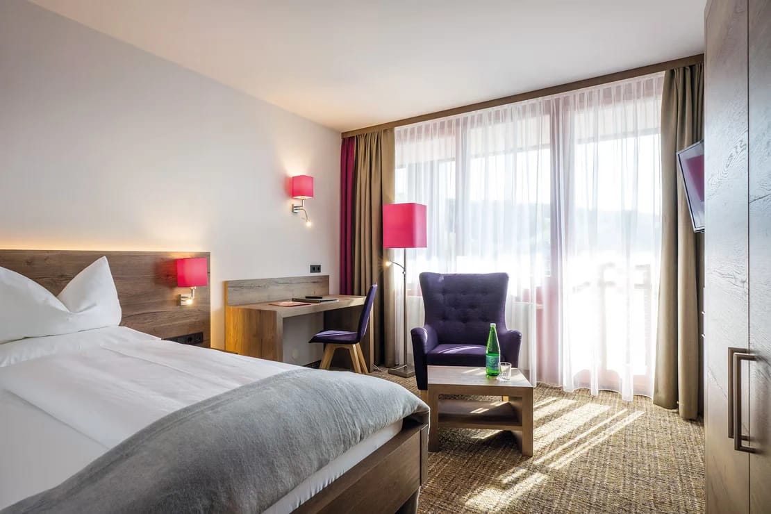Zimmer mit Bett, Sessel und großem Fenster mit Ausblick