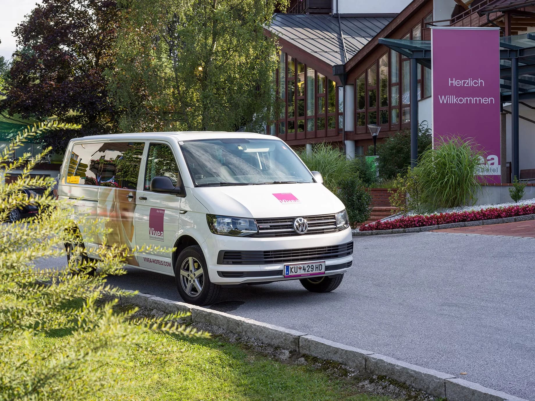 Hoteleingang mit Glasfront und Empfangsschild, davor der Vivea-Shuttlebus