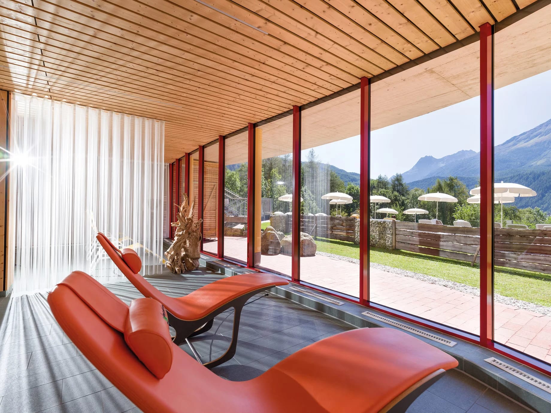 Ruheraum mit roten Relaxliegen und Panoramafenster zu den Bergen