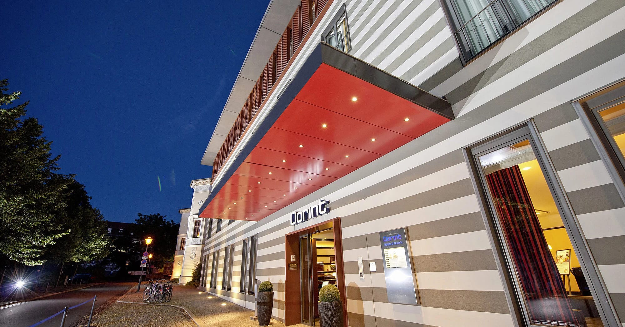 Beleuchtete Hotelfassade am Abend mit gestreifter Fassade und rotem Vordach