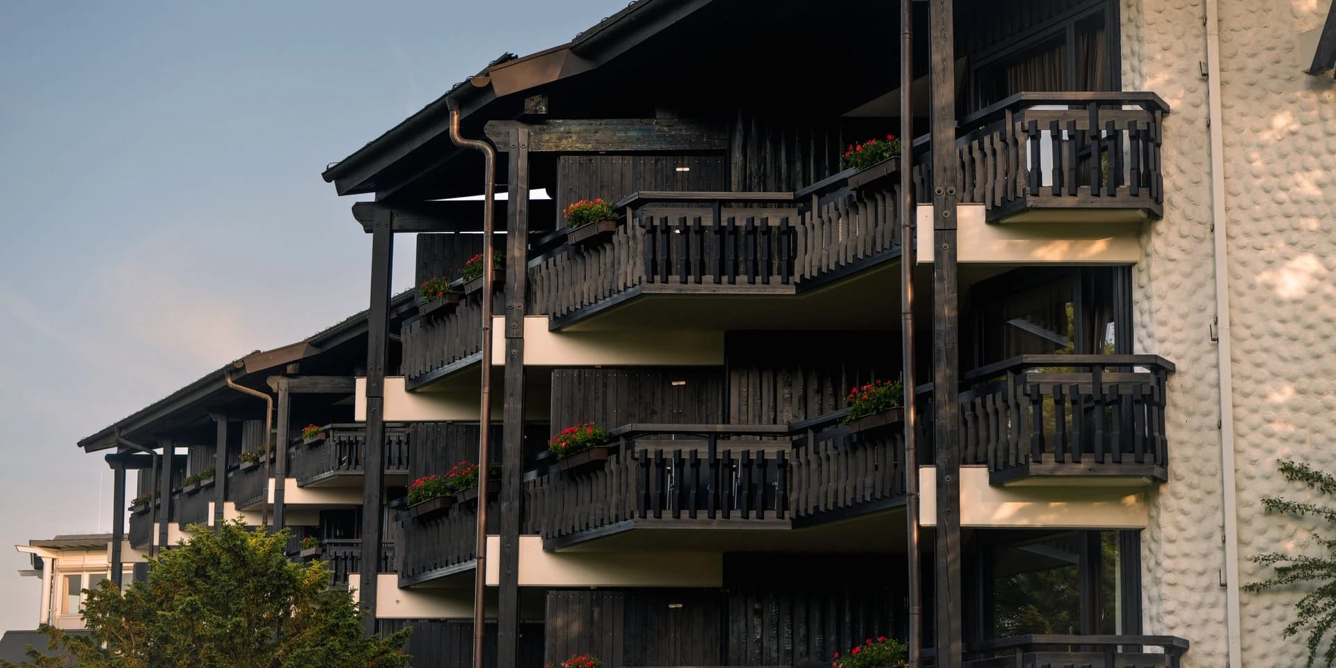 Dunkle Holzfassade des Hauses mit umlaufenden Balkonen und Blumenkästen im Abendlicht