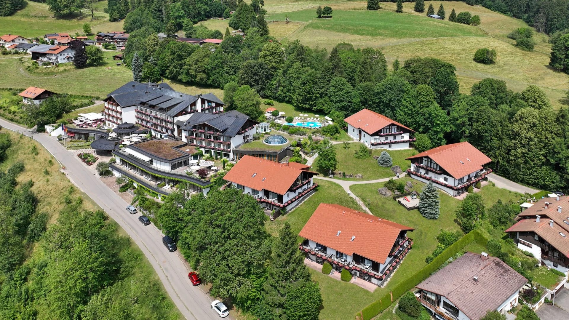 Luftbild des Hotels mit den Landhäusern, Außenpool und umliegenden Wiesen und Wäldern