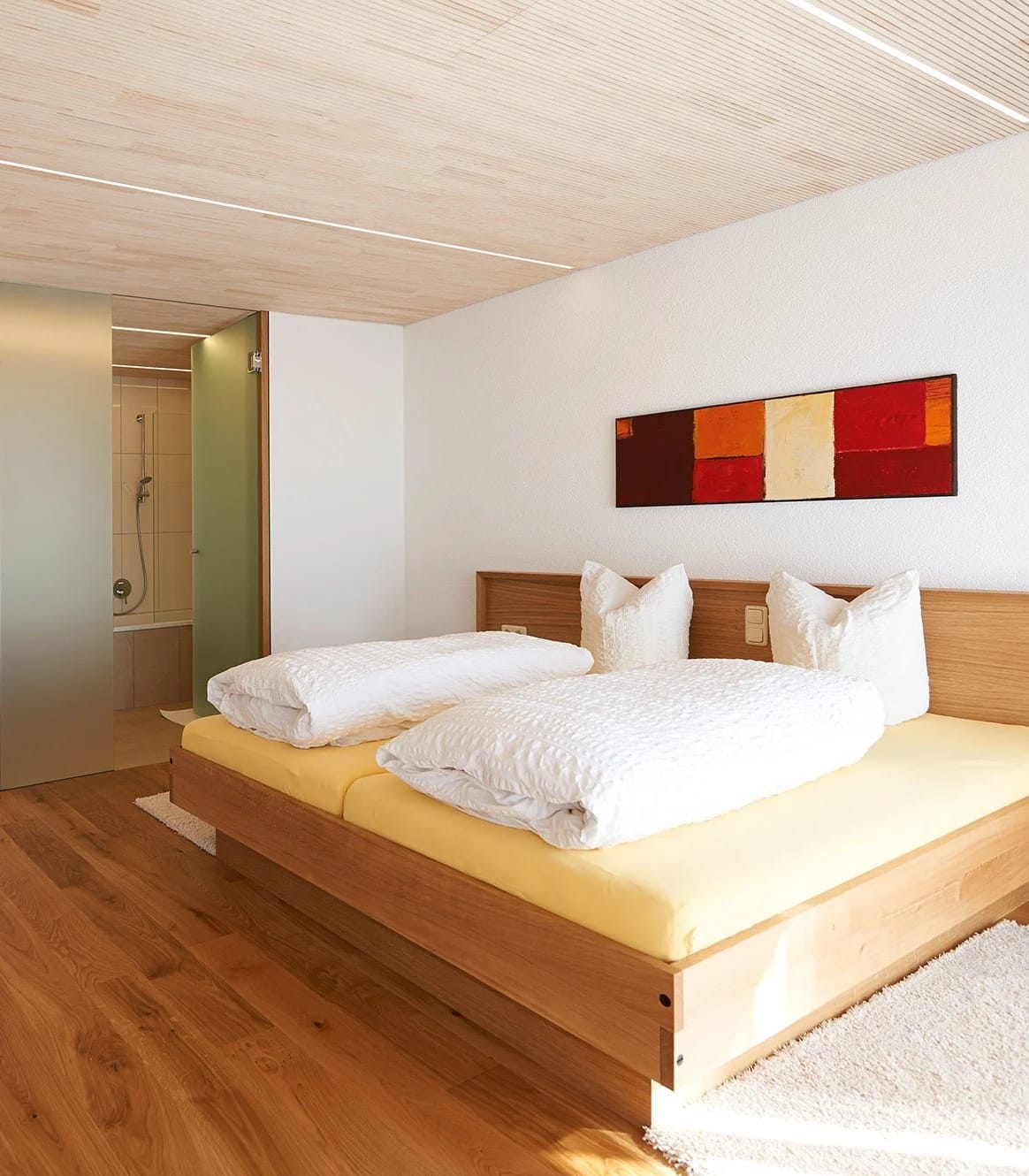 Zimmer mit zwei zusammengestellten Betten, heller Holzdecke und offenem Zugang zum Bad