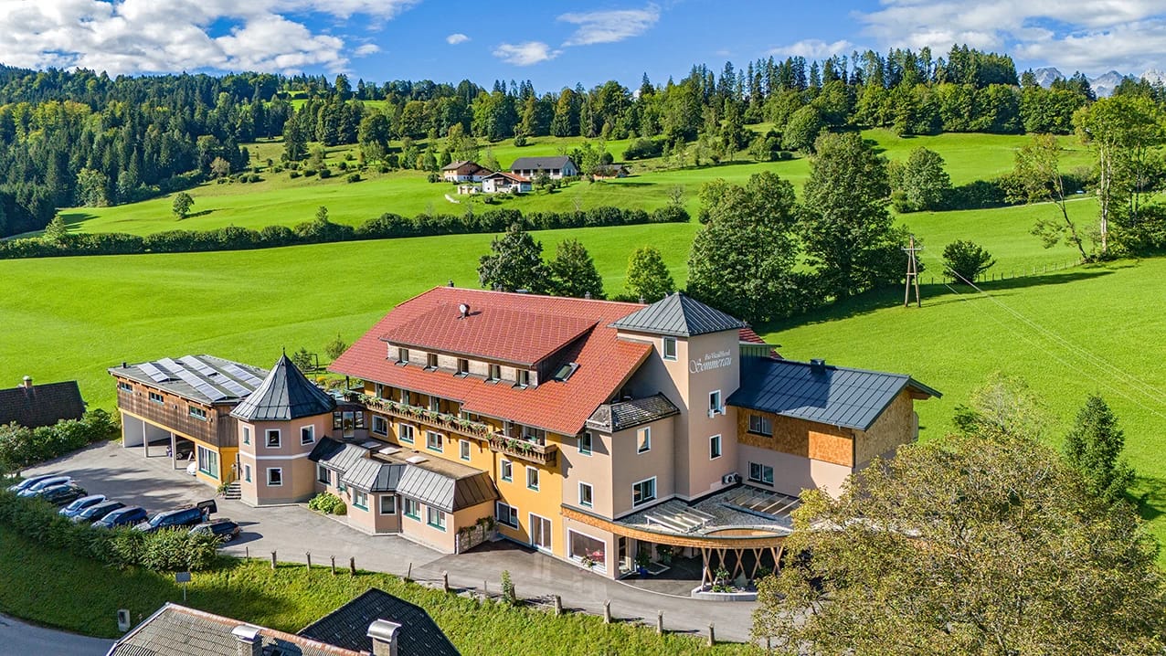 Luftaufnahme des Hotelgebäudes mit rotem Dach zwischen grünen Wiesen