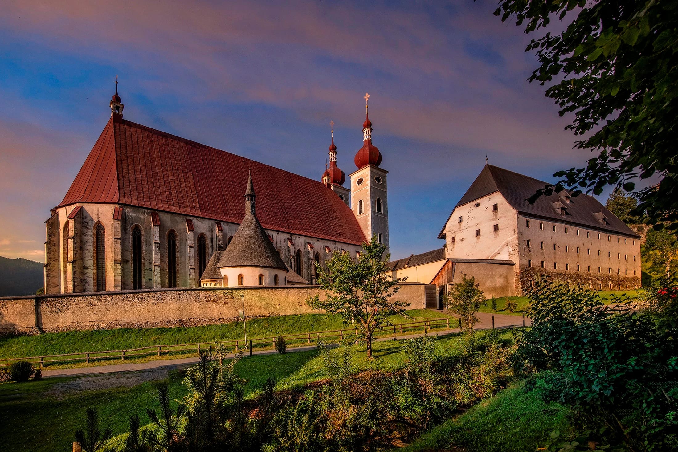 Stiftsanlage mit Kirche und Zwiebelturm im Abendlicht, von der Wiese aus gesehen
