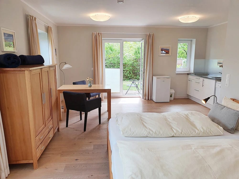 Heller Apartmentraum mit Bett, Schreibtisch, Kleiderschrank, Küchenzeile und Terrassentür zum Garten