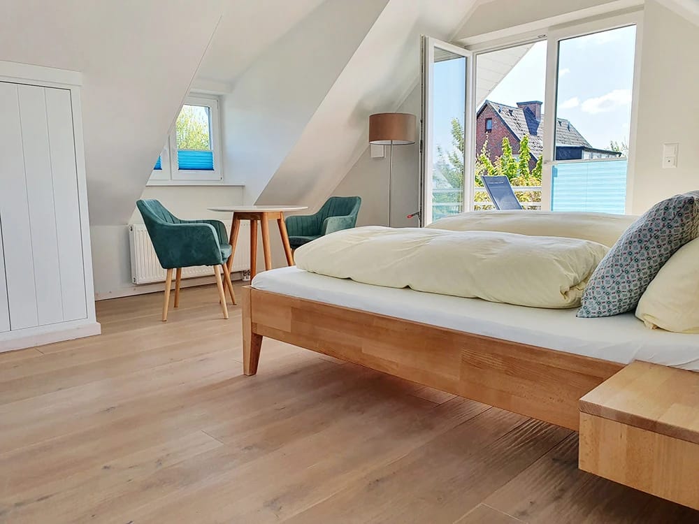 Dachgeschosszimmer mit Doppelbett, grünen Sesseln, kleinem Tisch und Fenstertür zum Balkon