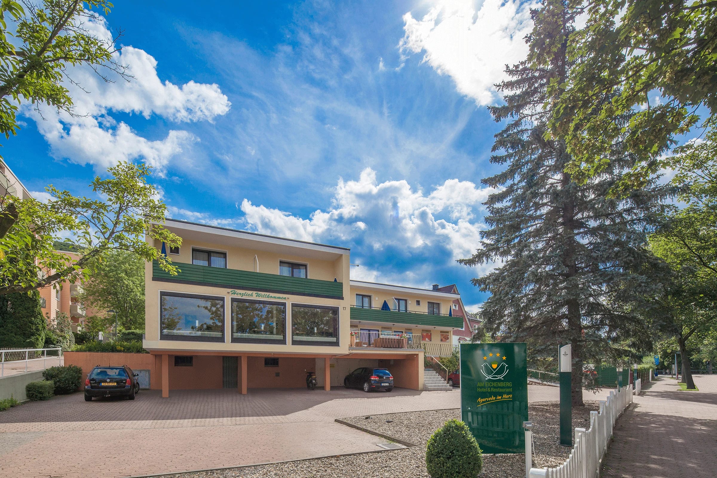 Außenansicht des Hotelgebäudes mit Vorfahrt, geparkten Autos und hohen Nadelbäumen