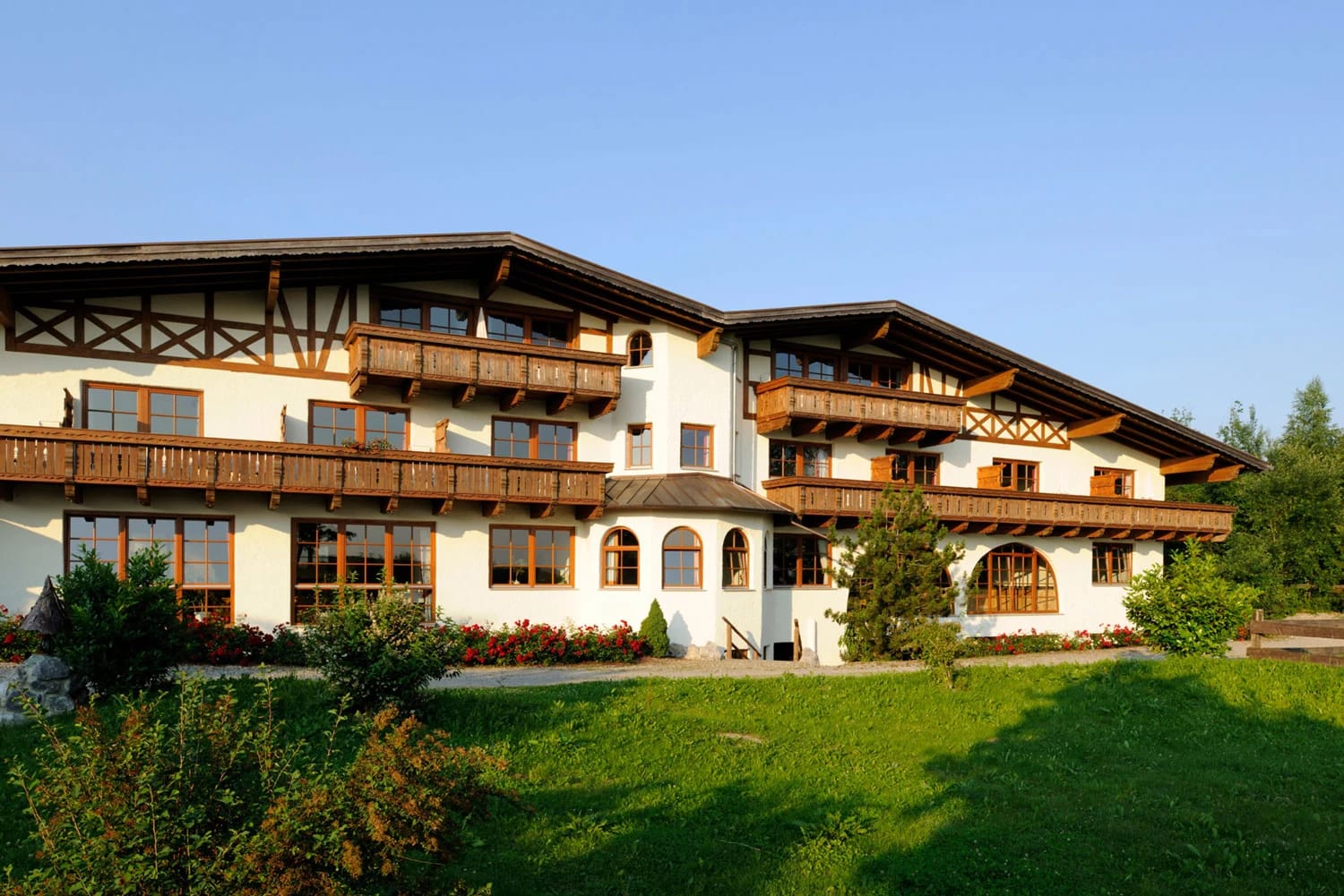 Außenansicht des Landhotels mit Holzbalkonen und grüner Wiese im Vordergrund