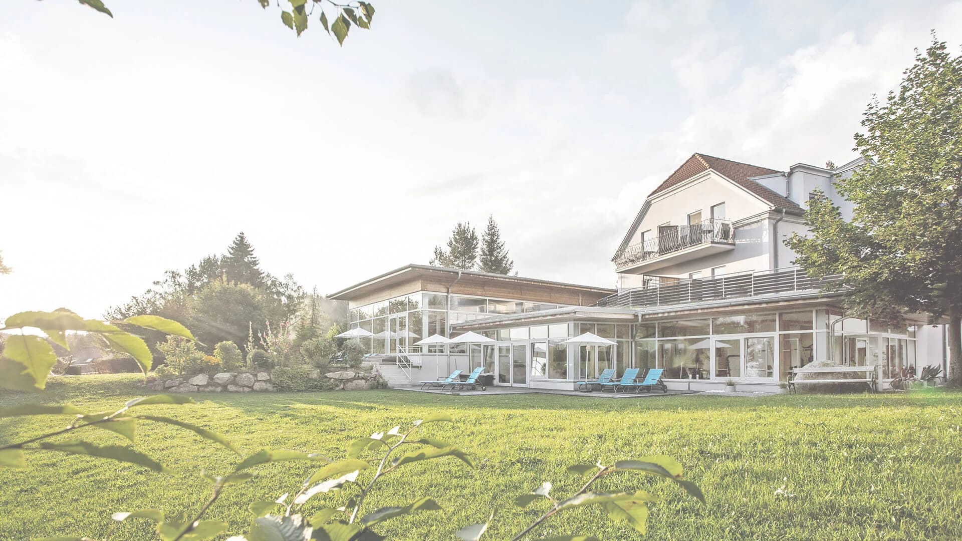 Außenansicht des Gesundheitshotels Klosterberg mit Glasfront, Sonnenterrasse und Gartenwiese im Sommer
