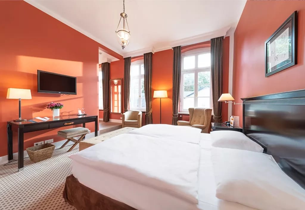 Hotelzimmer mit roter Wandfarbe, Doppelbett, Schreibtisch und Sessel am Fenster