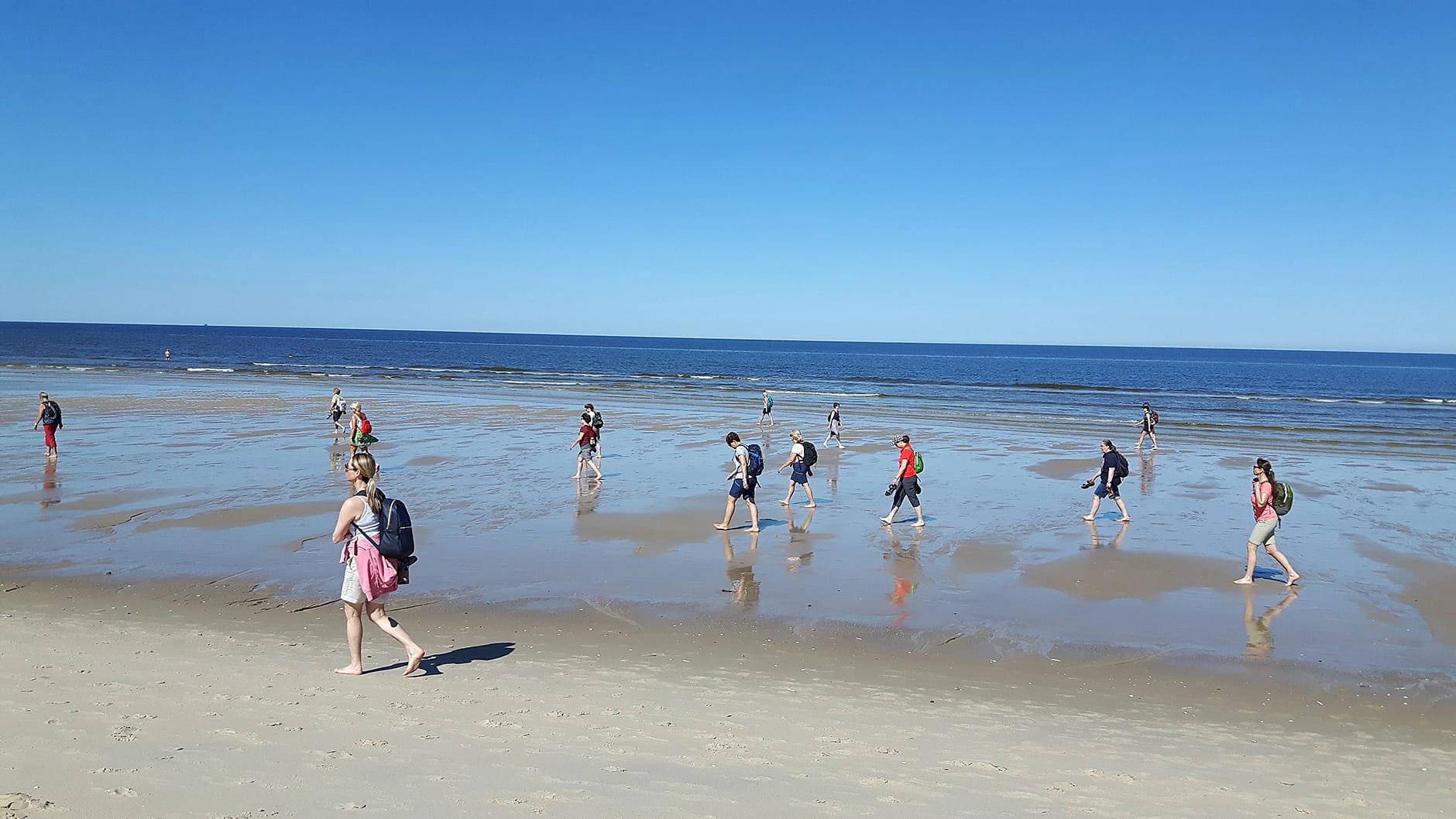 Wandergruppe am Strand bei Ebbe, dahinter das Meer unter blauem Himmel