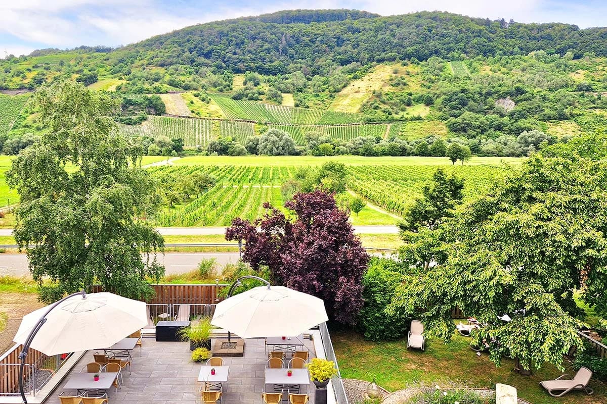 Blick von oben auf die Terrasse mit Sonnenschirmen und Sitzplätzen, dahinter die Weinberge