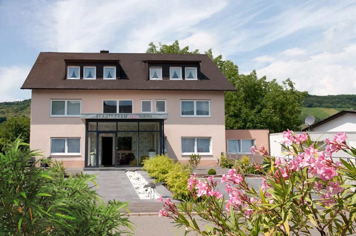 Außenansicht des Haupthauses mit verglastem Eingang, Hecken und blühendem Oleander im Vordergrund