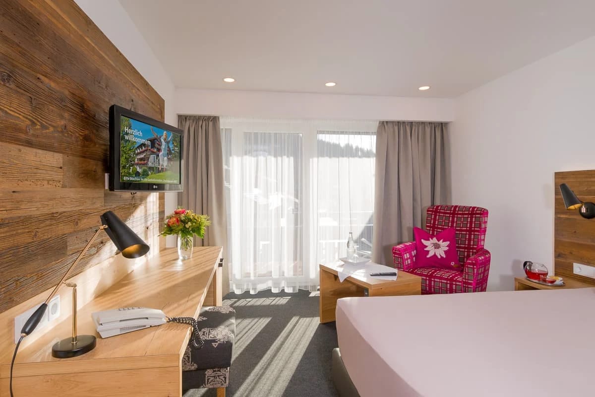 Modernes Einzelzimmer mit Altholzwand, Schreibtisch und Sessel am Balkonfenster