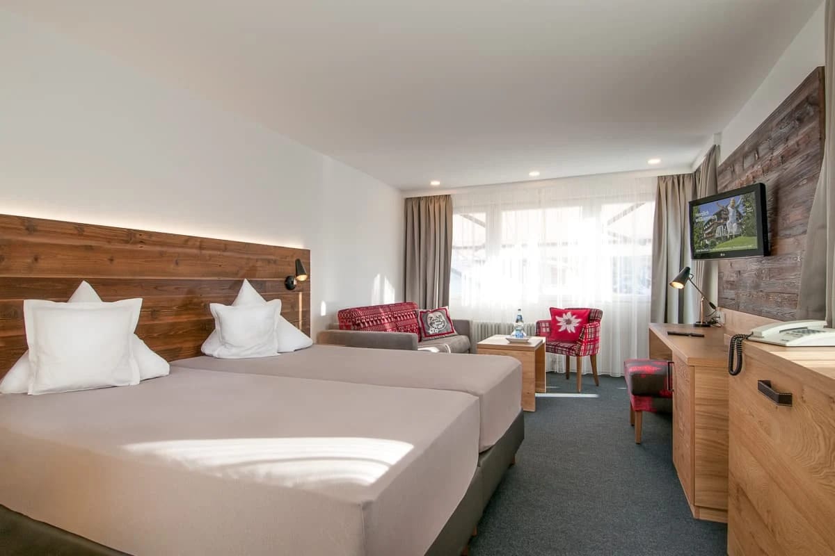 Doppelzimmer mit zwei Betten, Holzkopfteil und Sitzgruppe am Fenster