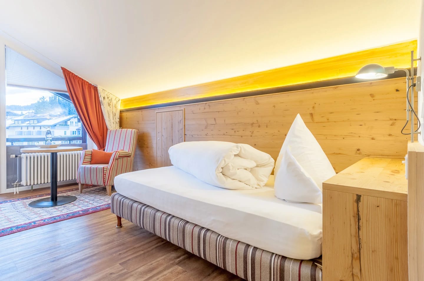 Studio mit Altholzwand und indirektem Licht, Einzelbett und Balkonfenster mit Bergblick