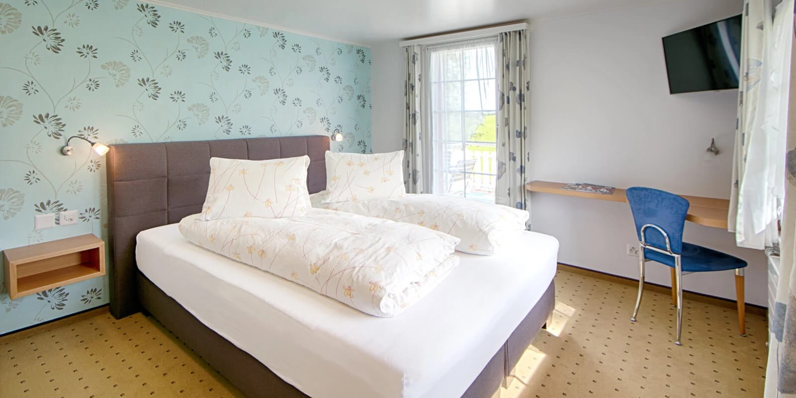 Doppelzimmer mit blau gemusterter Tapete und Doppelbett