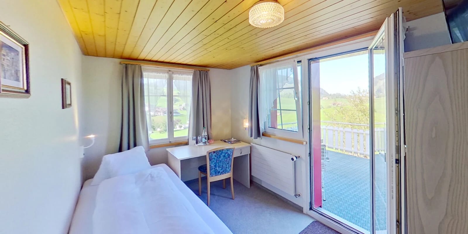 Helles Zimmer mit Bett, Schreibtisch und Balkontür mit Bergblick