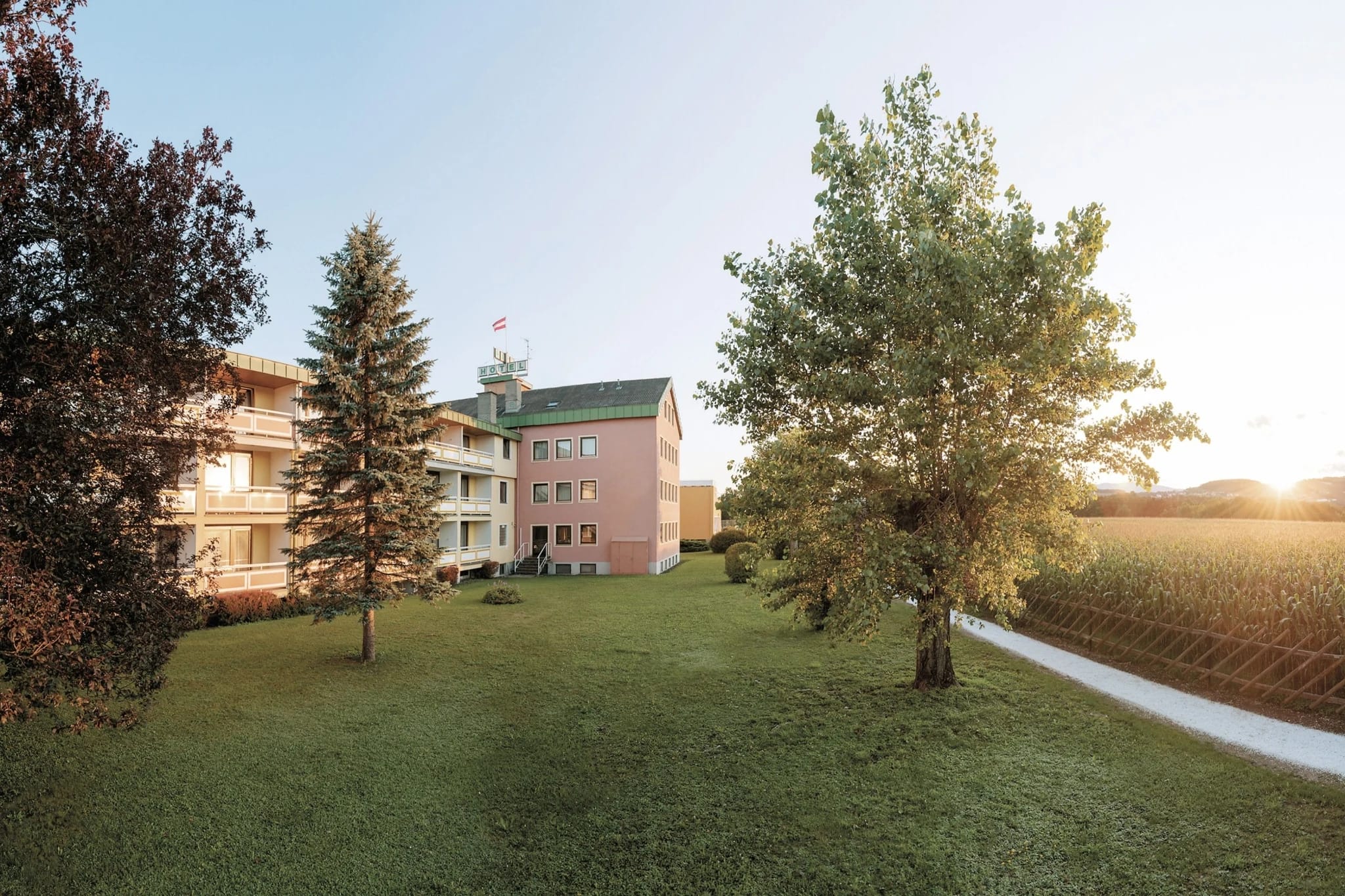 Außenansicht des Wilfinger Ring Bio Hotels mit weitläufigem Garten und Bäumen im Abendlicht