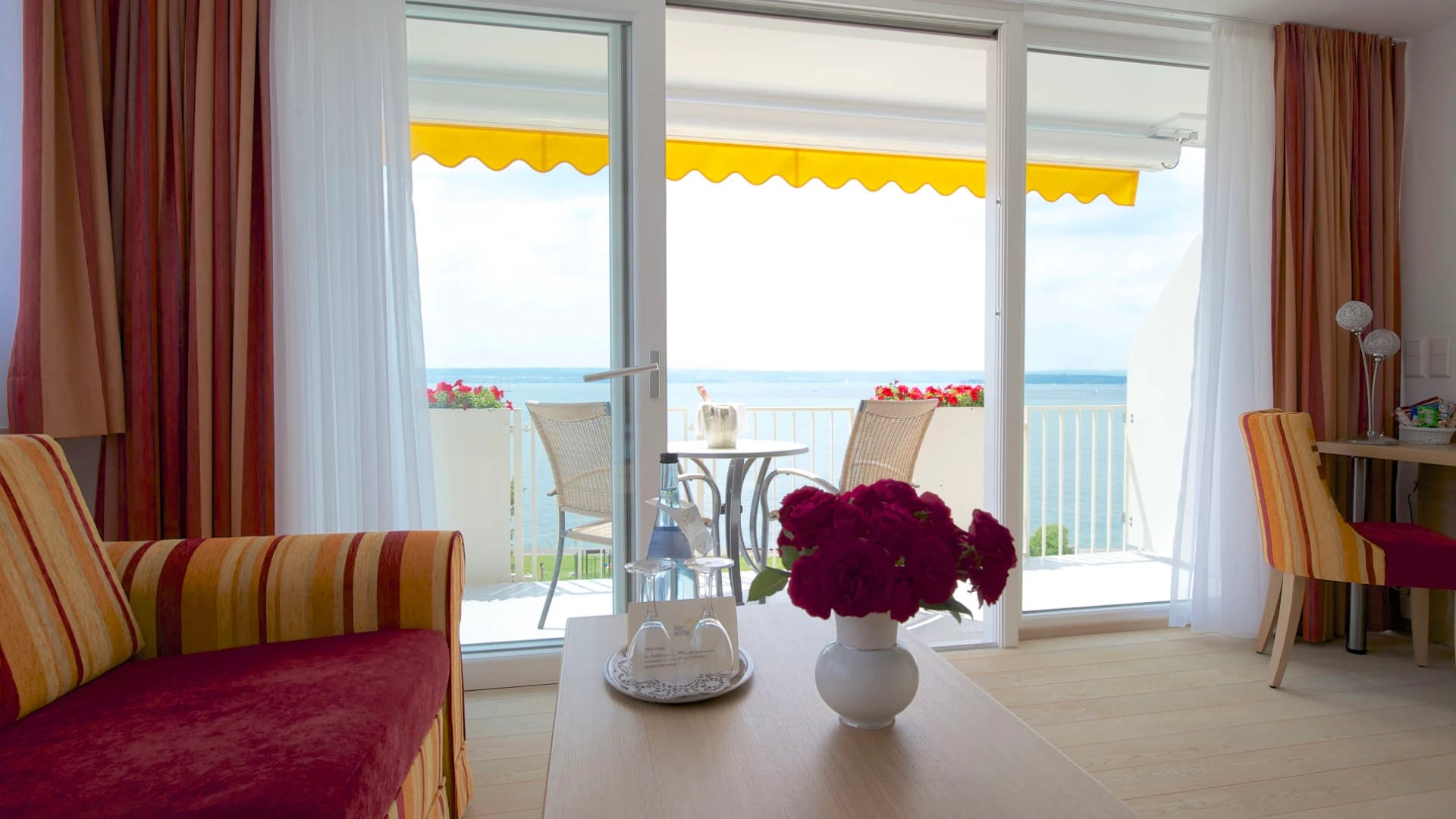Balkon mit Tisch, Korbstühlen und Blumenkästen, Blick über die Liegewiese auf den Bodensee