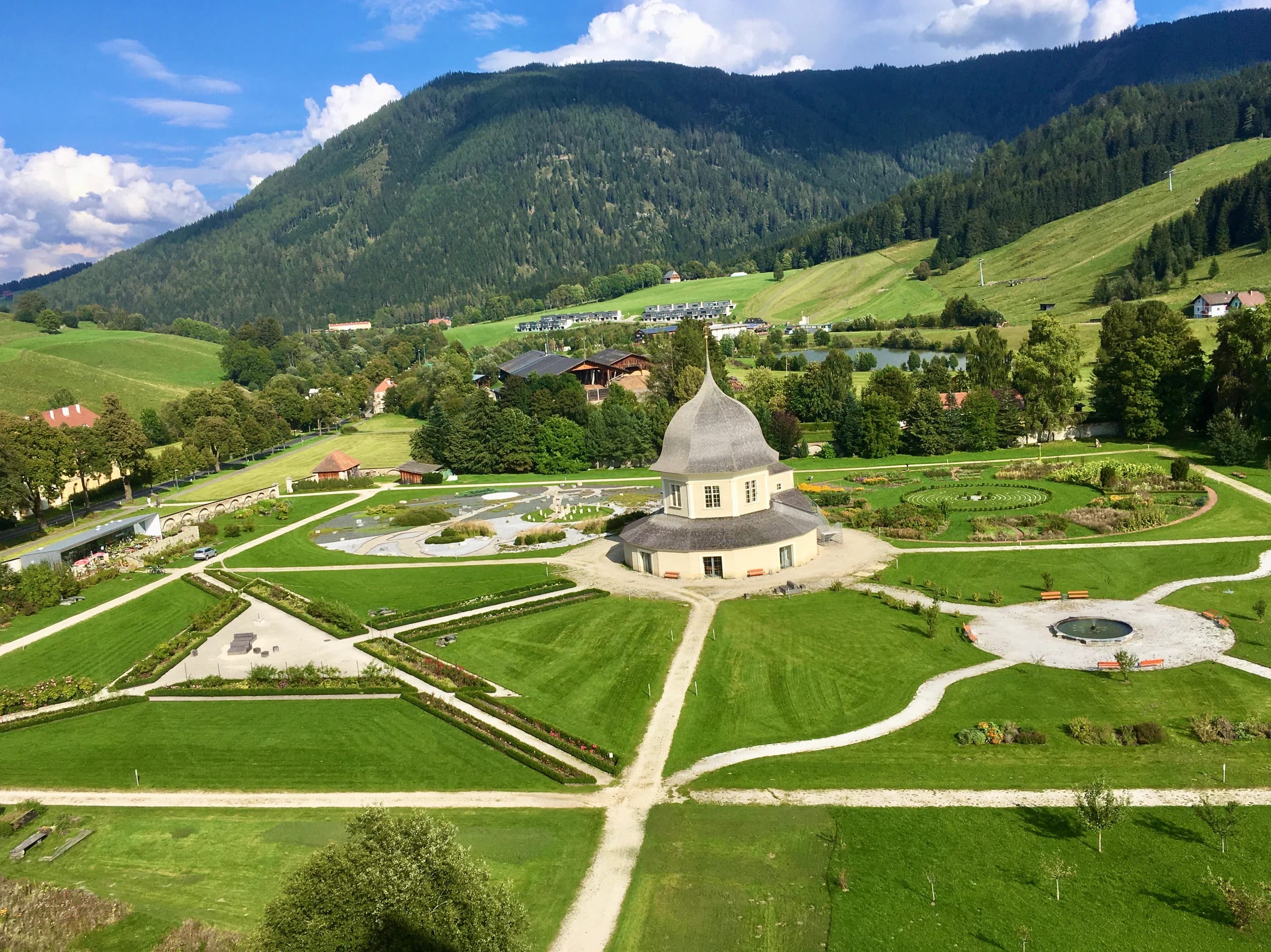 Blick von oben auf den Stiftsgarten mit Pavillon, Beeten und bewaldeten Bergen