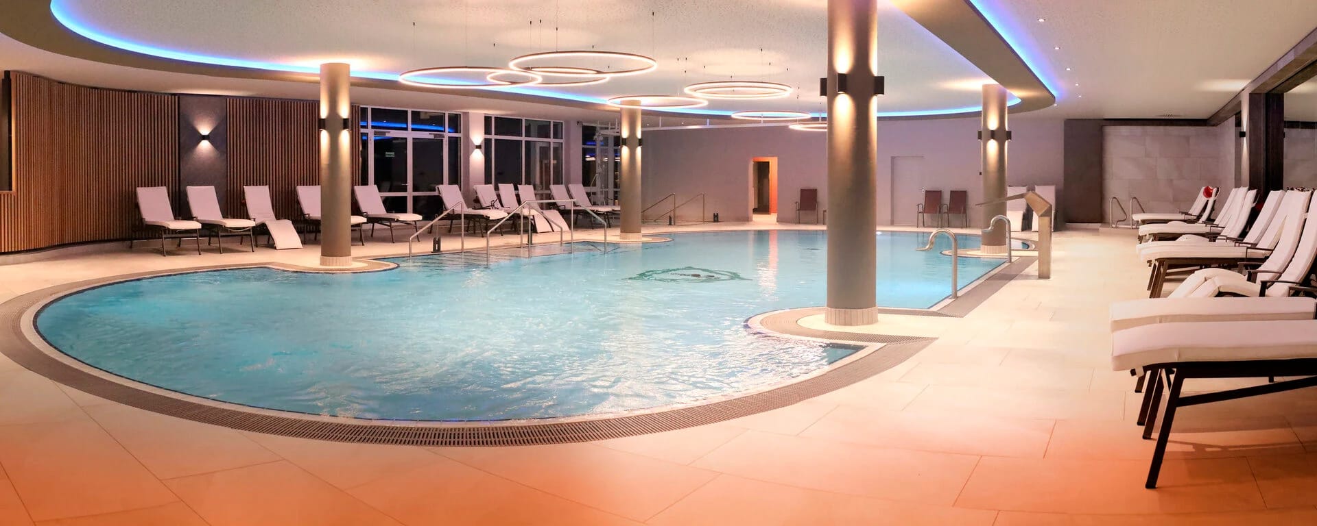 Thermal-Innenpool mit geschwungenem Beckenrand, Liegen an den Wänden und runden Deckenleuchten