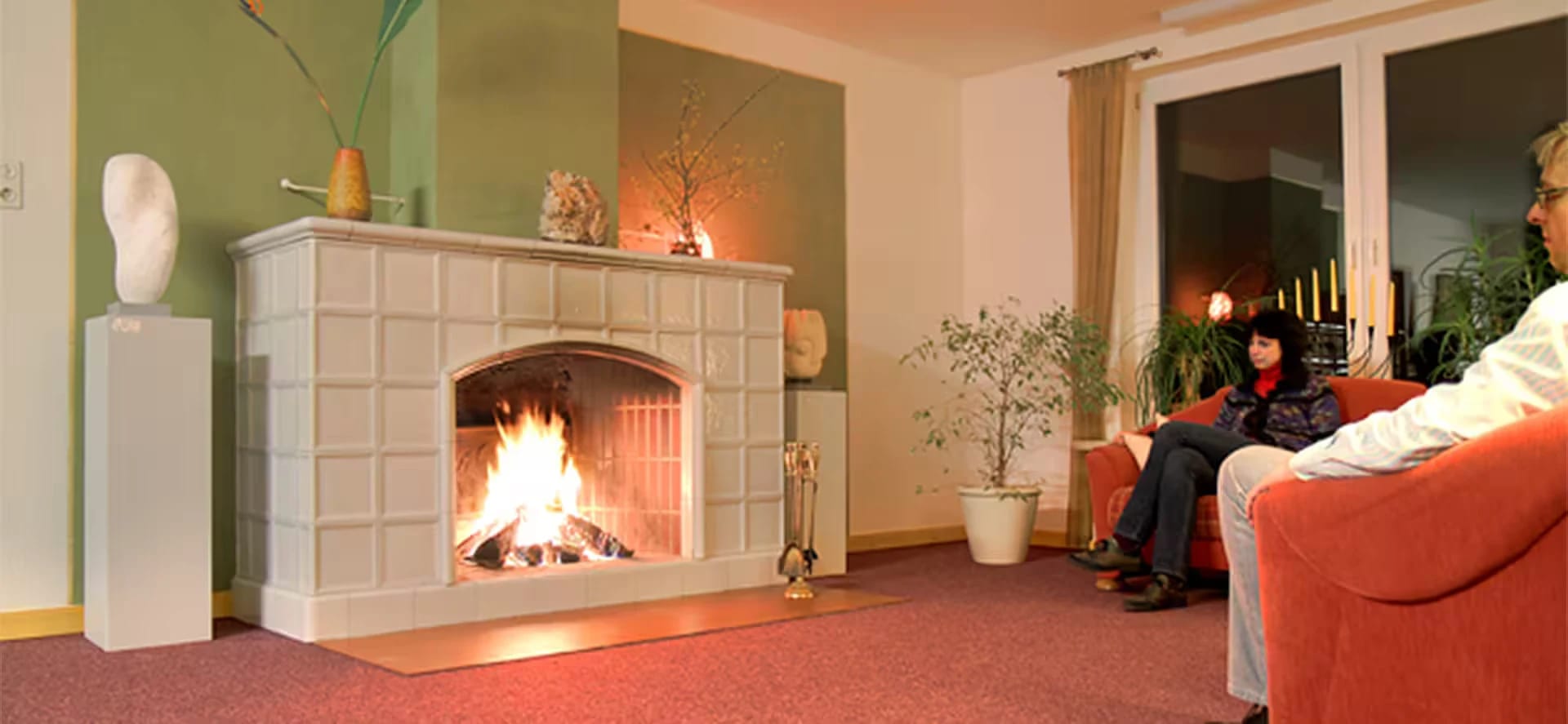 Kaminzimmer mit weißem Kachelkamin und brennendem Feuer