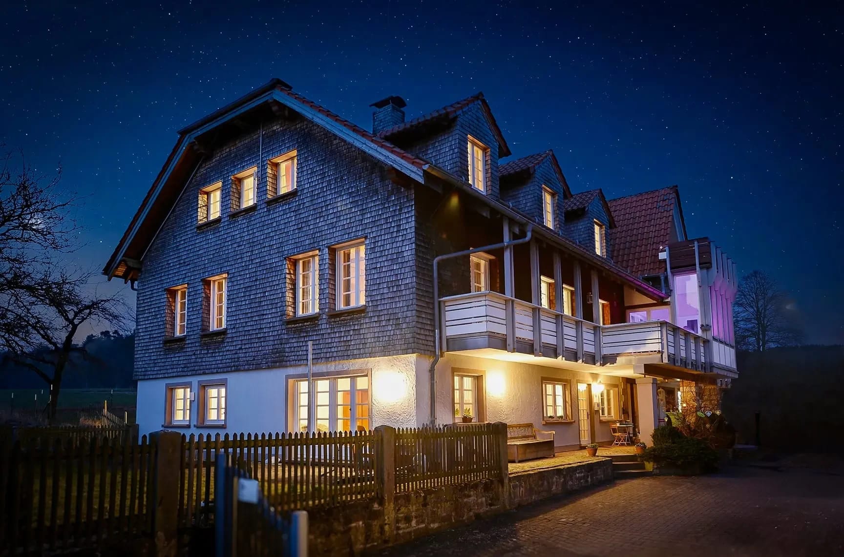 Beleuchtetes Haupthaus mit Schindelfassade und Balkon am Abend