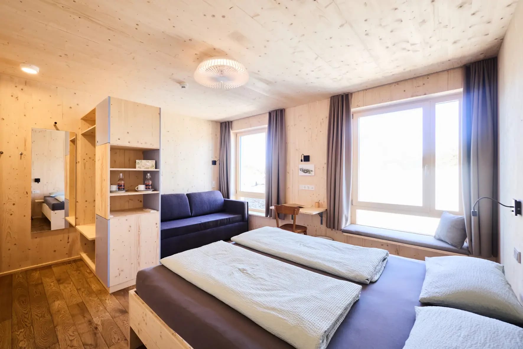 Zimmer mit Holzwänden, Doppelbett, Sofa und großem Fenster