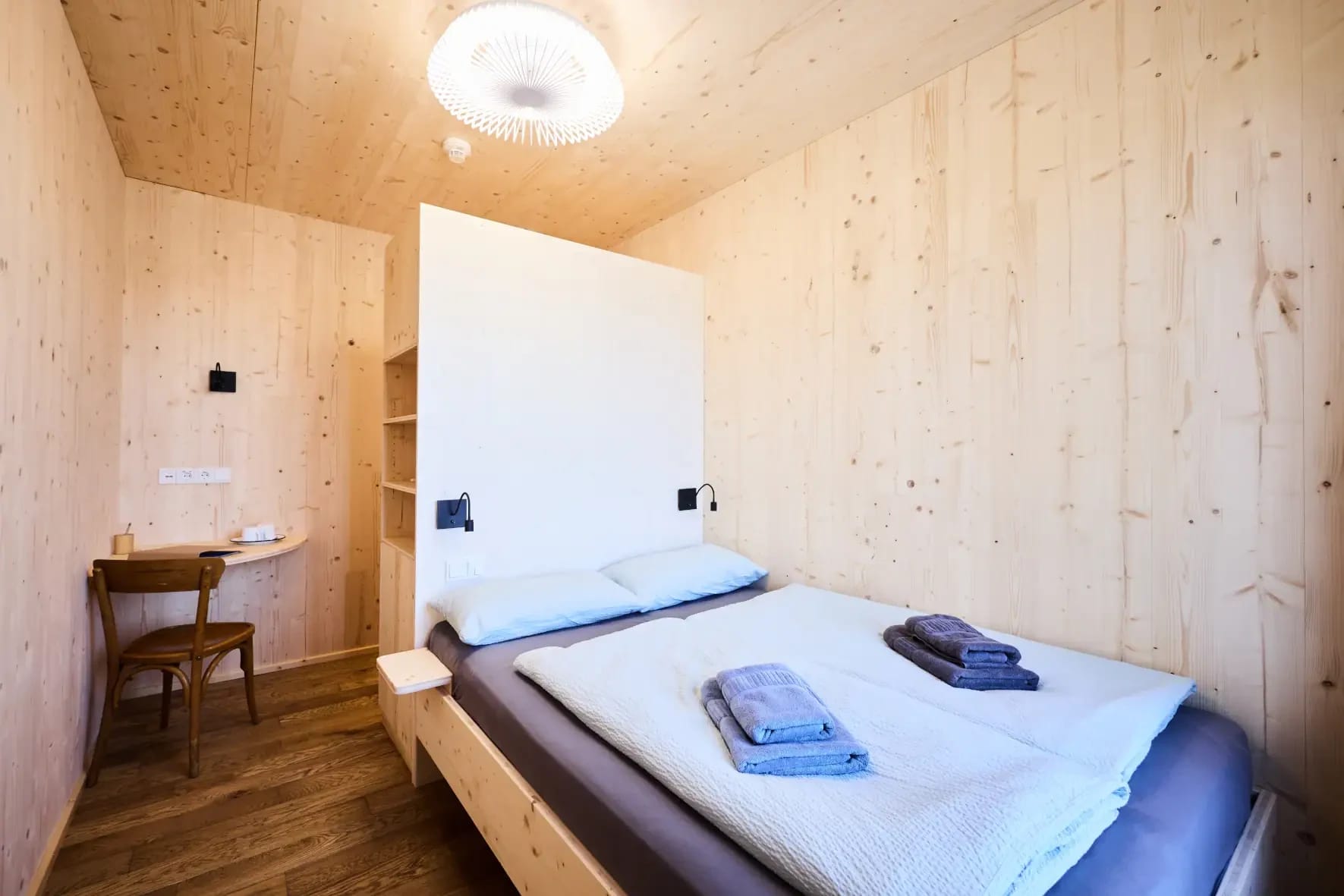 Holzverkleidetes Zimmer mit Doppelbett, Schreibtisch und Regalnische