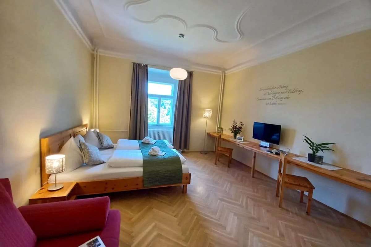 Großzügiges Zimmer mit Stuckdecke, Holzbett, Schreibtisch und rotem Sofa
