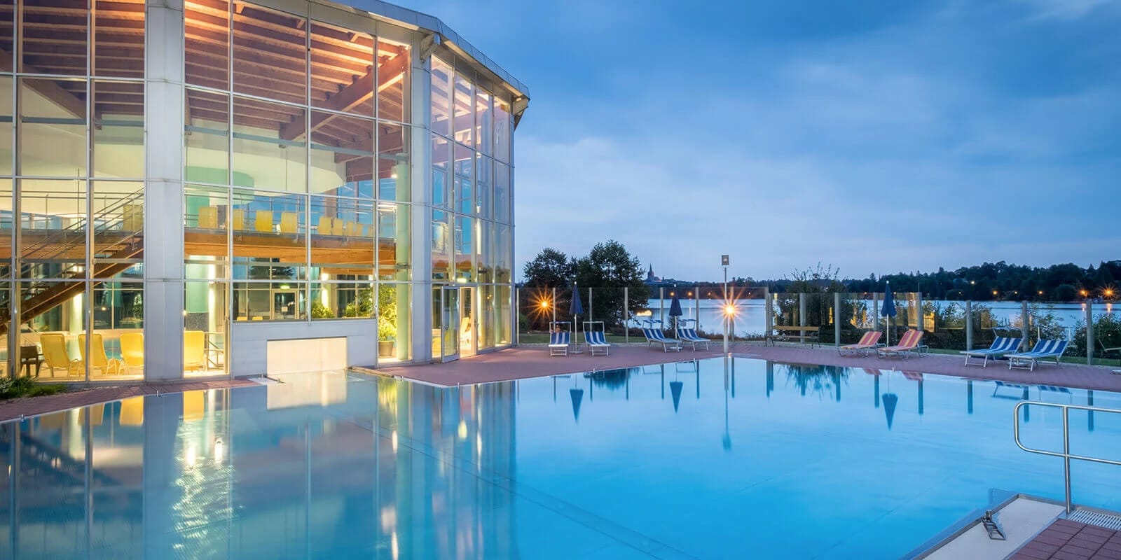 Beheiztes Außenschwimmbecken in der Abenddämmerung mit Blick auf den See